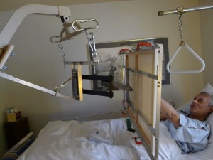 Figure 1: Photo of client using the device from his bed.  The Reliant lift base is on the upper left of the photo, below that is the hanging support, and in the middle of the photo is the TV mount and easel system.