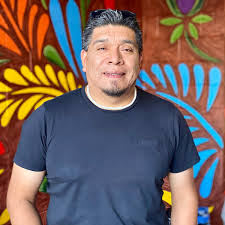 Man in blue shirt with grey hair in front of a brightly color mural