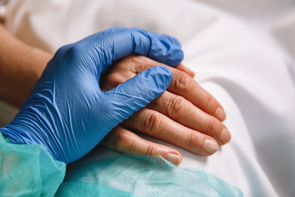 Closeup of healthcare worker wearing blue gloves holding a patient's hand.