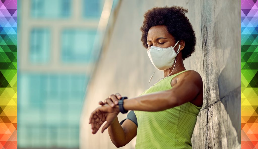 A masked woman takes a break from exercising outdoors to look at her smartwatch