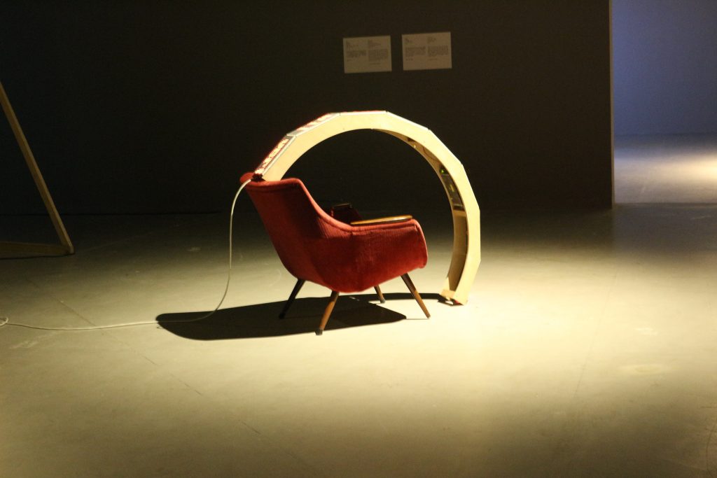 A chair with a semi-circle of screens protruding from the top and ending just before the ground.