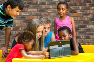 Multiracial group of children looking at tablet outdoors.