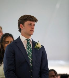 angled shot of Davis looking off camera wearing a navy suit, green tie and a white flower boutonniere 