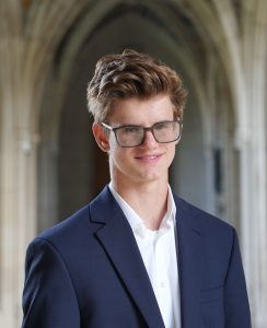 head shot of Grant wearing a blue blazer and white shirt with Duke arches in the background