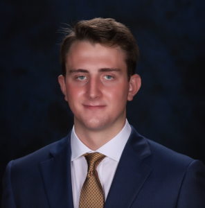 headshot of John wearing a navy suit and yellow tie