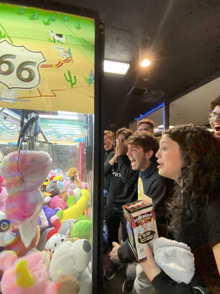 A group of students cheer on someone getting a prize from an arcade claw machine