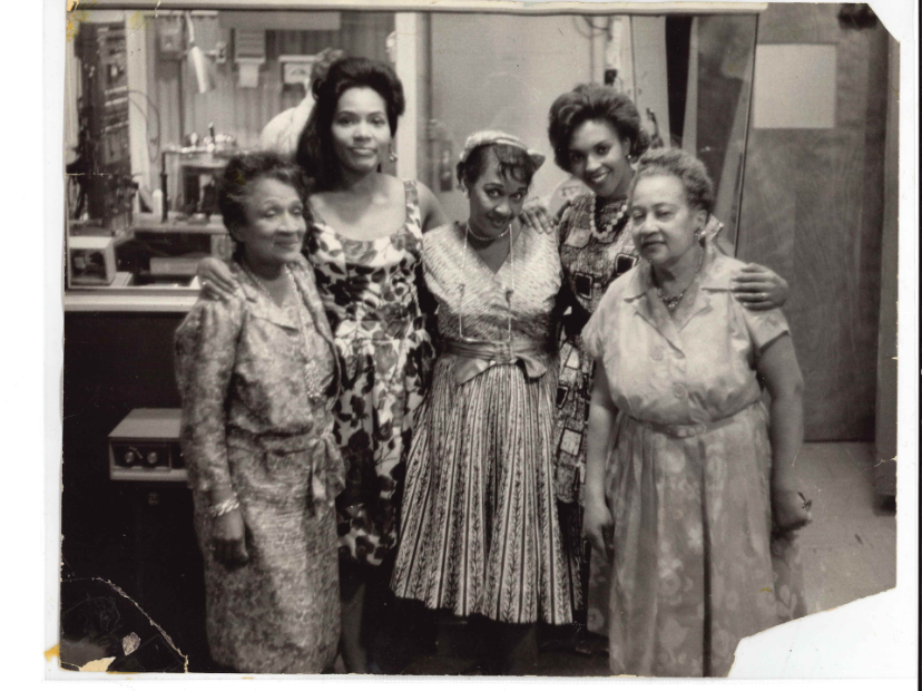 Five women stand close together and smile at the camera.