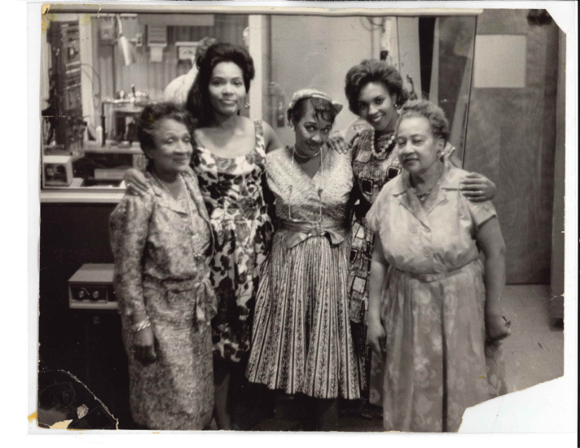 Five women stand close together and smile at the camera.